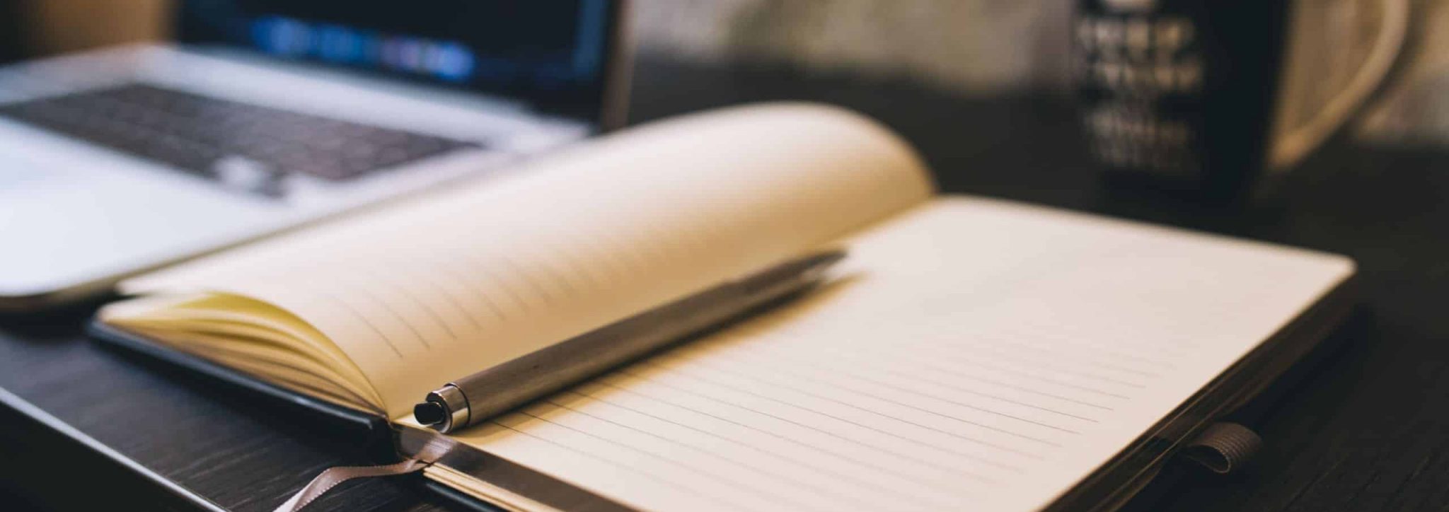 An open notebook next to a computer and coffee.